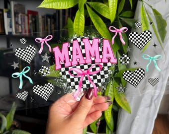 Puede incluir: Letrero acrílico transparente con la palabra "MAMA" en rosa, sobre un fondo a cuadros blanco y negro. El diseño incluye lazos rosas y turquesas, corazones a cuadros y estrellas.