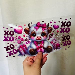 May include: A Valentine's Day themed graphic featuring a cute cartoon cow with a pink bow, holding a heart-shaped gift. Pink hearts and the text "XO" are scattered around the cow. The cow has brown and white fur and is surrounded by pink gifts and flowers.