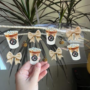 May include: A clear sticker sheet featuring coffee cup illustrations with the text "Seven Brew Coffee", tan bows, and coffee bean accents. The coffee cups have a white base and a brown top with ice.
