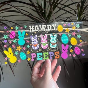 May include: A clear sticker sheet with the text "HOWDY my PEEPS" and Easter-themed graphics. The design includes colorful bunny rabbits, Easter eggs, and floral accents in shades of pink, yellow, blue, and purple. The sticker sheet is held up by a hand.