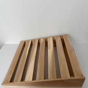 Peut inclure: Un casier à vin en bois avec un design à lattes. Le casier est en bois de couleur claire et a une forme rectangulaire avec des côtés inclinés. Les lattes sont espacées uniformément, créant une solution de stockage visuellement attrayante et fonctionnelle pour les bouteilles de vin.
