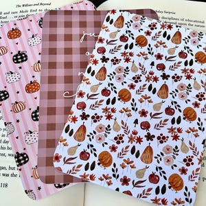 May include: Three rectangular bookmarks with rounded corners. One features a pink striped background with black and orange pumpkins. The second has a brown and white checkered pattern. The third displays a white background with orange pumpkins, pears, and flowers.
