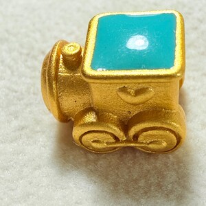 May include: A gold-coloured miniature train with a turquoise roof. The train has detailed wheels and a rounded front. The turquoise roof has a glossy finish. The train is likely a decorative item or charm.