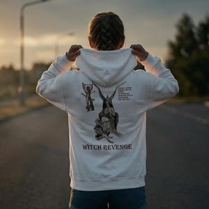 Puede incluir: Sudadera con capucha blanca con un diseño gráfico en la espalda. El diseño incluye ilustraciones y el texto "WITCH REVENGE". La sudadera tiene una capucha con cordón y mangas largas.