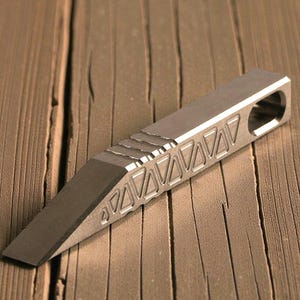 May include: A silver metal pry bar with a beveled edge and a triangular pattern. The tool has a rectangular body with a hole at one end. The pry bar is designed for leverage and prying.