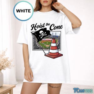 May include: White t-shirt with the text "Hoist the Cone" and a graphic of a pirate flag with a skull and crossbones, a red and white traffic cone, and a baseball field. The shirt has short sleeves.