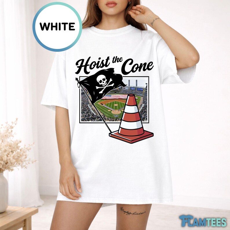 May include: White t-shirt with the text "Hoist the Cone" and a graphic of a pirate flag with a skull and crossbones, a red and white traffic cone, and a baseball field. The shirt has short sleeves.