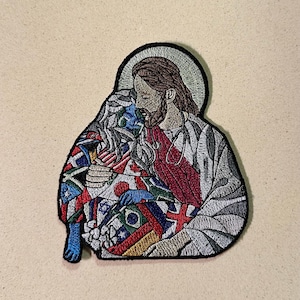 May include: Embroidered patch depicting a religious figure embracing another figure covered in flags. The patch has a black border, with the figures in shades of brown, red, white, blue, and grey. The flags represent various countries.