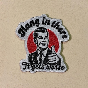 May include: Embroidered patch featuring a smiling man giving a thumbs up inside a red circle. The patch reads "Hang in there" above the image and "It gets worse" below, all in a retro style.