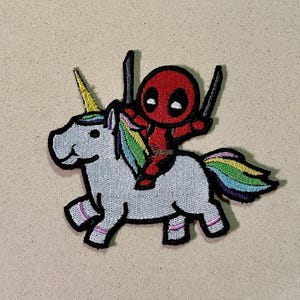 Peut inclure: Écusson brodé représentant un personnage de dessin animé Deadpool chevauchant une licorne. La licorne est blanche avec une crinière et une queue arc-en-ciel, et le personnage de Deadpool est rouge avec des accents noirs et tient deux épées. Le patch a une bordure noire.