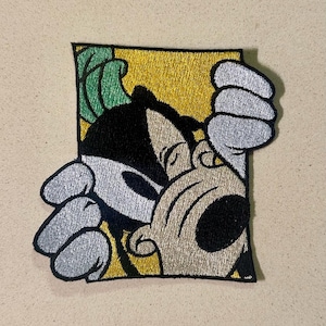 May include: Embroidered patch depicting a cartoon character emerging from a yellow and black rectangle. The character has black and white features, with silver hands and green details. Suitable for application on clothing or accessories.