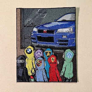 May include: Embroidered patch featuring a blue Nissan Skyline GT-R car and figures in hooded jackets with car brand logos. The logos include Audi, BMW, Porsche, Ferrari, and Volkswagen. The Nissan logo is visible.
