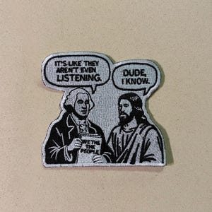 以下が含まれることがあります： ジョージ・ワシントンとイエス・キリストの漫画風デザインの刺繍パッチ。「IT'S LIKE THEY AREN'T EVEN LISTENING」と「DUDE, I KNOW」という吹き出し。ワシントンは「WE THE PEOPLE」と書かれた本を持っています。