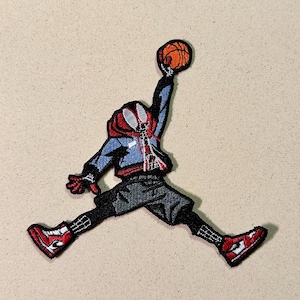 Può includere: Toppa ricamata raffigurante una figura stilizzata in posa da basket, che tiene una palla. La figura indossa una giacca blu, una felpa con cappuccio rossa e pantaloncini neri, con scarpe da ginnastica rosse e bianche. La toppa ha un tema di Spider-Man.