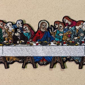 Peut inclure: Écusson brodé représentant la Cène. L'image montre des personnages assis autour d'une table, avec Jésus au centre. Le patch a une nappe blanche et les personnages sont vêtus de différentes couleurs.