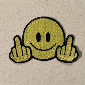 May include: Yellow smiley face patch with black outline and two middle fingers raised. The patch has a textured appearance and is set against a neutral background. The design is a humorous and bold statement.