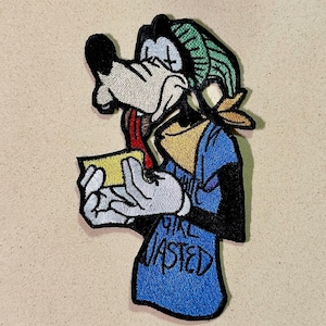 Pode incluir: Patch bordado com um personagem de cachorro de desenho animado em uma camisa azul com o texto "Girl Wasted". O cachorro tem um gorro verde, um lenço amarelo e está segurando um objeto amarelo. O patch é preto, branco, azul, amarelo e verde.