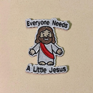 May include: Embroidered patch depicting a cartoon Jesus with brown hair and a beard, wearing a white robe and a red sash. The patch includes the text "Everyone Needs A Little Jesus" in a stylized font.
