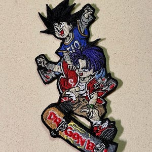 Puede incluir: Parche bordado con dos personajes de anime montados en monopatín. El parche tiene un diseño colorido con las palabras "Dragon Ball" en el monopatín. Los personajes visten ropa deportiva.