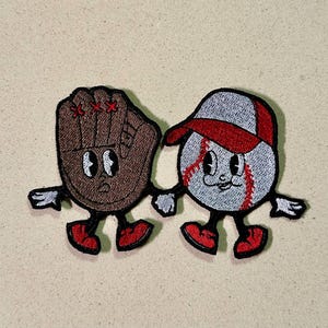 Può includere: Toppa ricamata raffigurante una palla da baseball e un guanto da baseball, entrambi con facce da cartone animato e che si tengono per mano. La palla da baseball è grigia con cuciture rosse e un berretto rosso. Il guanto è marrone con cuciture rosse.