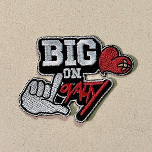 Puede incluir: Parche bordado con las palabras "BIG ON LOYALTY" en blanco, rojo y negro. El diseño incluye un gesto de la mano, un corazón y la palabra "BIG" en negrita. El parche tiene un borde negro.