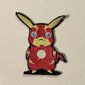 Peut inclure: Écusson brodé représentant un mélange de Pikachu et de Flash. Le design est principalement rouge et jaune, avec des yeux bleus et un emblème d'éclair blanc. L'écusson a une bordure noire et est destiné aux vêtements ou accessoires.