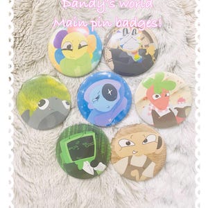 May include: Seven circular pin badges featuring colorful cartoon character illustrations. The text Dandy's world Main pin badges! is printed at the top. The designs include a yellow flower, a clock-themed character, a gray creature, a blue figure, a strawberry-like character, a green television head, and a tan character.
