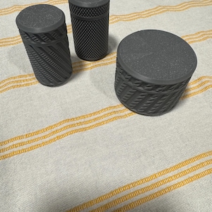May include: Three gray containers with textured surfaces. Two are cylindrical, one with a diagonal stripe pattern and the other with a grid pattern. The third is a round, basket-weave style container. All have matching lids.
