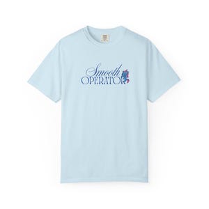 May include: Light blue t-shirt with the words "Smooth Operator" in a script font. A small graphic of a seahorse is next to the word "Operator". The shirt is made of a soft material.