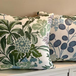 May include: Two decorative throw pillows with floral patterns. One pillow features a white background with green and blue floral designs. The other pillow has a white background with blue and green floral designs.