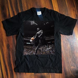 May include: Black t-shirt featuring a graphic of Darth Vader playing basketball. The image is in black and white, with a basketball hoop and a crowd in the background. The shirt has the signature "D. Vader" on the graphic.