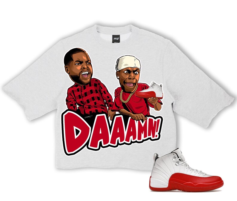 Puede incluir: Una camiseta gris claro con un gr&aacute;fico de dos personajes de dibujos animados y la palabra "DAAAMN!" en rojo. Un par de zapatillas blancas y rojas est&aacute;n en la imagen. La camiseta tiene cuello redondo y mangas cortas.