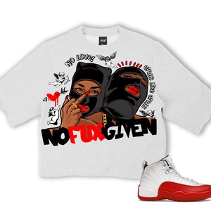 Puede incluir: Una camiseta gris claro de gran tama&ntilde;o con un gr&aacute;fico que presenta dos figuras con pasamonta&ntilde;as negros, labios rojos y cadenas doradas. La camiseta tiene el texto "NO LOVE! GIRLS LIKE GIRLS STOP GIVEN" y "NO FUX GIVEN". Una zapatilla deportiva blanca y roja est&aacute; en la parte inferior derecha.