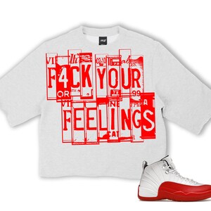 Puede incluir: Una sudadera gris claro de gran tama&ntilde;o con las palabras "F4CK YOUR FEELINGS" en letras rojas. Una zapatilla de baloncesto blanca y roja est&aacute; en la esquina inferior derecha.