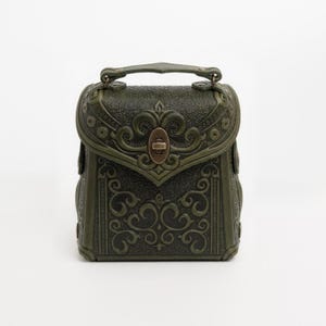 May include: A dark green, ornate handbag with a top handle and a decorative clasp. The bag features embossed scrollwork and a rectangular shape. The overall design has a vintage or antique aesthetic.