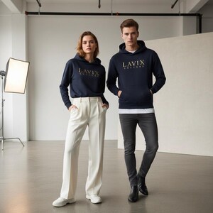 May include: Two people wearing navy blue hoodies with the gold text "LAVIX COUTURE". The person on the left is wearing white pants and sneakers. The person on the right is wearing dark gray jeans and black boots. The background is a white studio.
