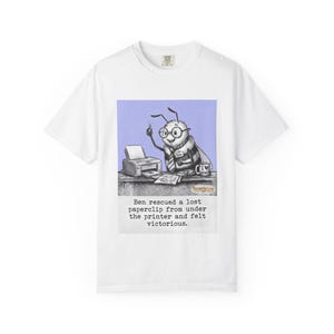May include: White t-shirt featuring a cartoon bee wearing glasses and a name tag that says "Ben." The bee is depicted at a desk with a printer and the text "Ben rescued a lost paperclip from under the printer and felt victorious."