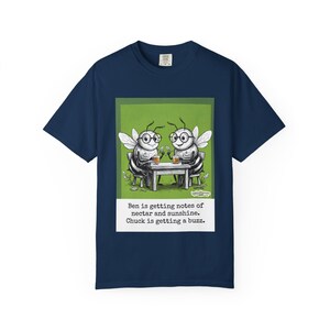 May include: Navy blue t-shirt featuring a cartoon illustration of two bees at a table, wearing glasses and drinking. The text reads, "Ben is getting notes of nectar and sunshine. Chuck is getting a buzz."