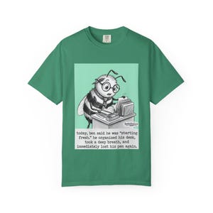 May include: Green t-shirt featuring a cartoon bee wearing glasses and working at a desk. The image includes the text: "today, ben said he was 'starting fresh,' he organized his desk, took a deep breath, and immediately lost his pen again."
