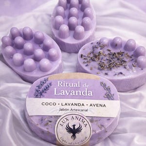 May include: Four lavender artisan soaps with different textures. One soap has rounded bumps, another has dried herbs, and a third has the text "Ritual de Lavanda". The soaps are on a white, silky surface.