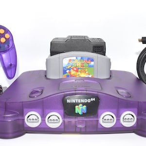 May include: A translucent purple Nintendo 64 game console with a matching purple controller, a Super Mario 64 game cartridge inserted, and a black AV cable. Two small grey rectangular blocks with the text TinkerTech by MR are also included.