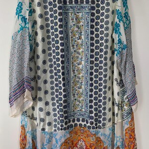 May include: A long, flowing kimono-style garment with a vibrant, eclectic design. The piece features a mix of patterns, including floral, geometric, and paisley motifs in shades of blue, orange, and white. The kimono has long sleeves and a relaxed fit.