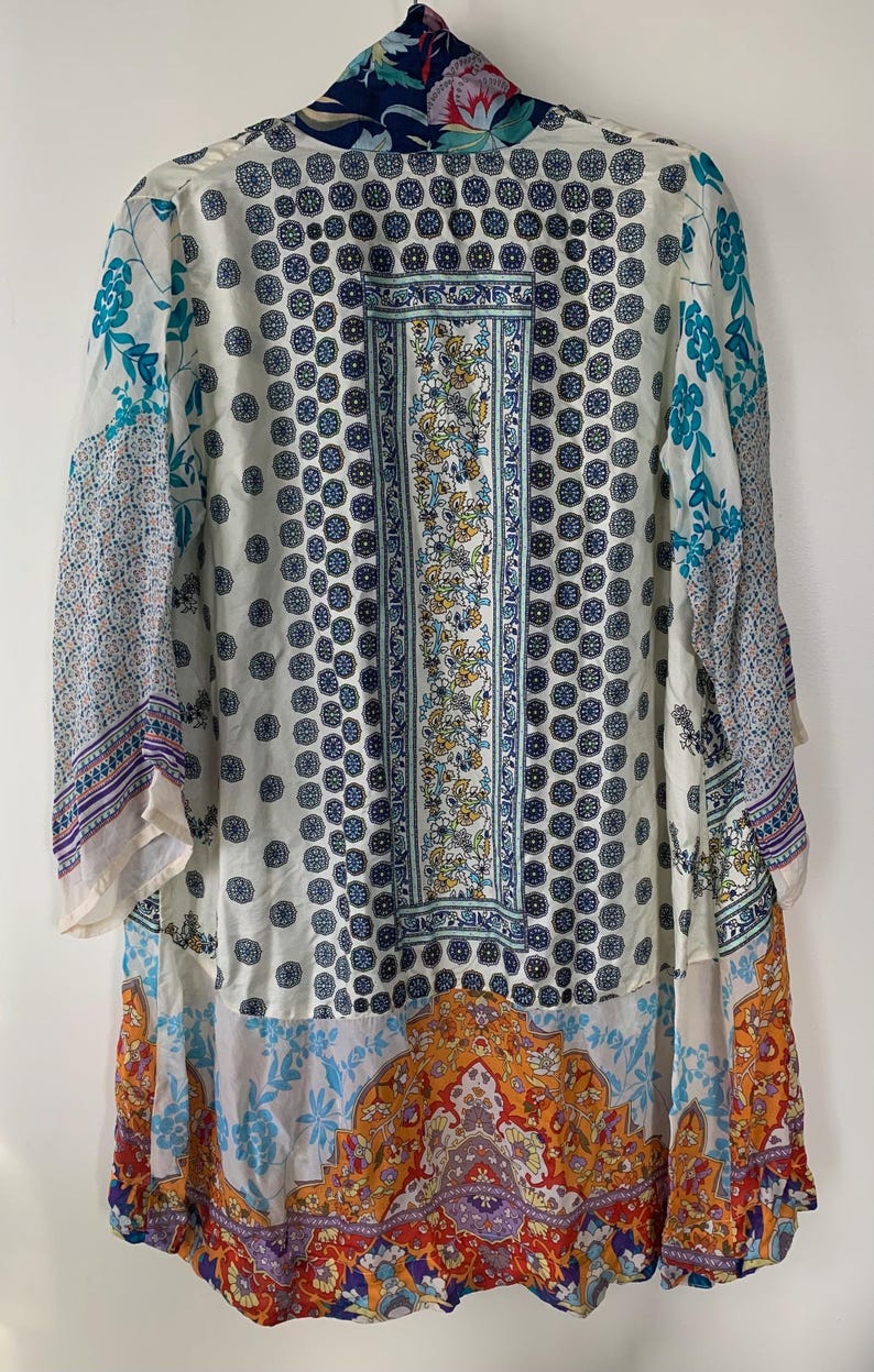 May include: A long, flowing kimono-style garment with a vibrant, eclectic design. The piece features a mix of patterns, including floral, geometric, and paisley motifs in shades of blue, orange, and white. The kimono has long sleeves and a relaxed fit.