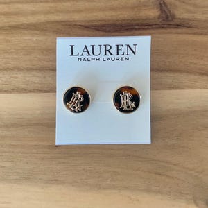 May include: A pair of round stud earrings with a gold-tone border and a tortoiseshell pattern center. The earrings feature a gold monogram design. The earrings are displayed on a white card with the "LAUREN RALPH LAUREN" logo.