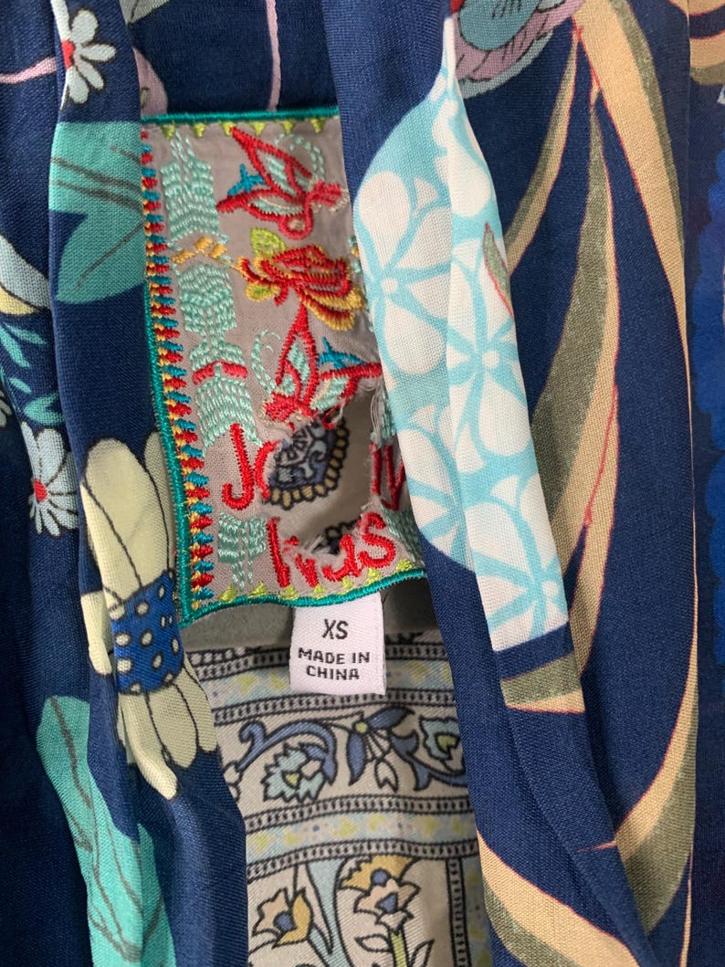 May include: Close-up of a navy blue garment with a floral pattern. The garment features an embroidered label with the text "Jus Iris" and a size tag that reads "XS". The garment is made in China.