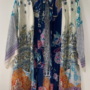 May include: A long, open-front kimono-style robe with a patchwork design. The robe features a mix of floral and paisley patterns in shades of blue, orange, white, and purple. The sleeves are three-quarter length, and the robe has two front pockets.