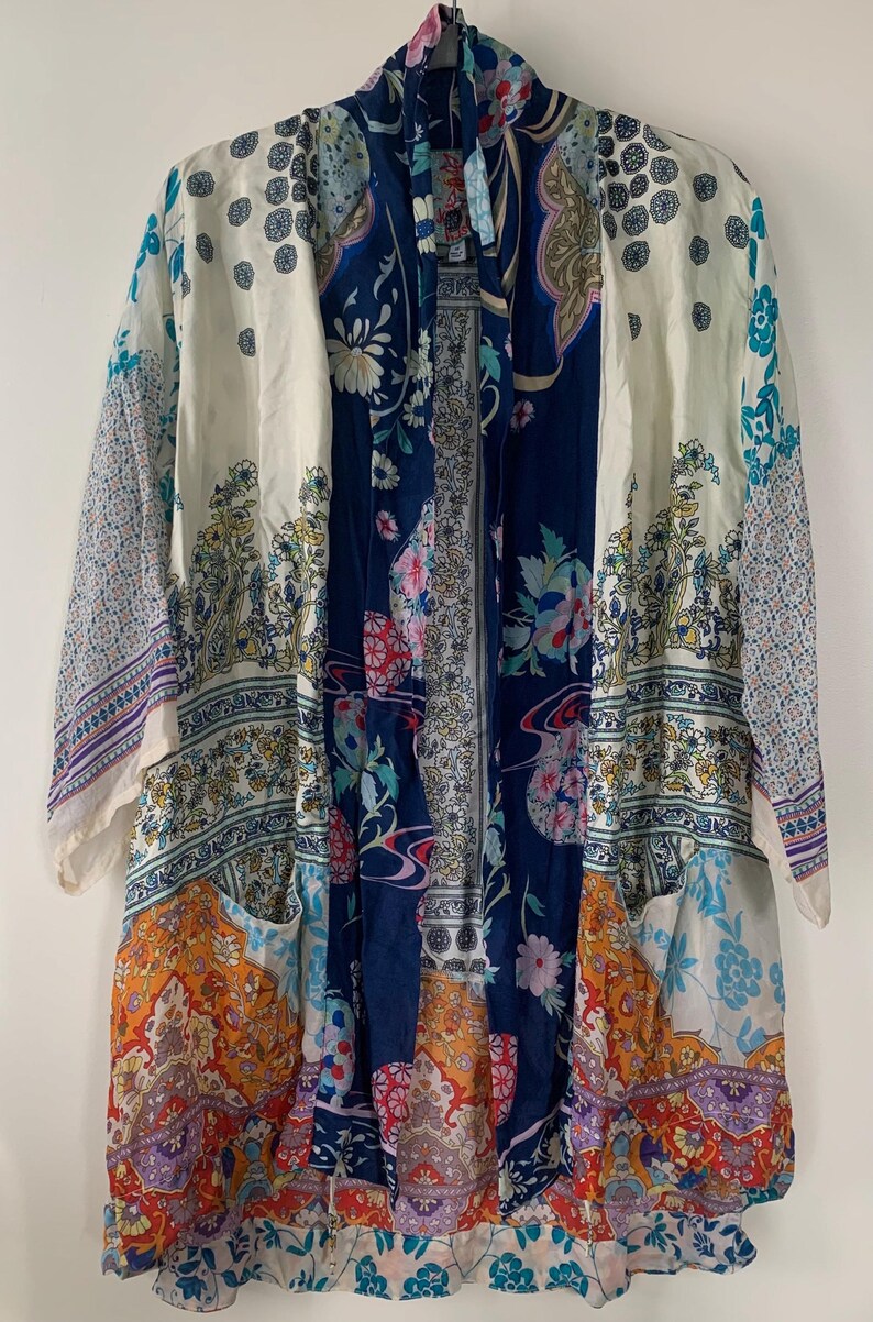 May include: A long, open-front kimono-style robe with a patchwork design. The robe features a mix of floral and paisley patterns in shades of blue, orange, white, and purple. The sleeves are three-quarter length, and the robe has two front pockets.