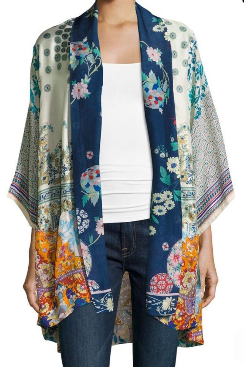 May include: A colorful kimono-style garment with a floral pattern. The open-front design features a navy blue panel with floral designs, complemented by cream and orange patterned sections. The sleeves have a patterned border.