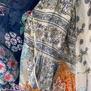 May include: A patchwork garment featuring a variety of floral and paisley patterns in shades of blue, white, orange, and purple. The garment appears to be made of lightweight fabric, possibly a kimono or a similar style of cover-up.
