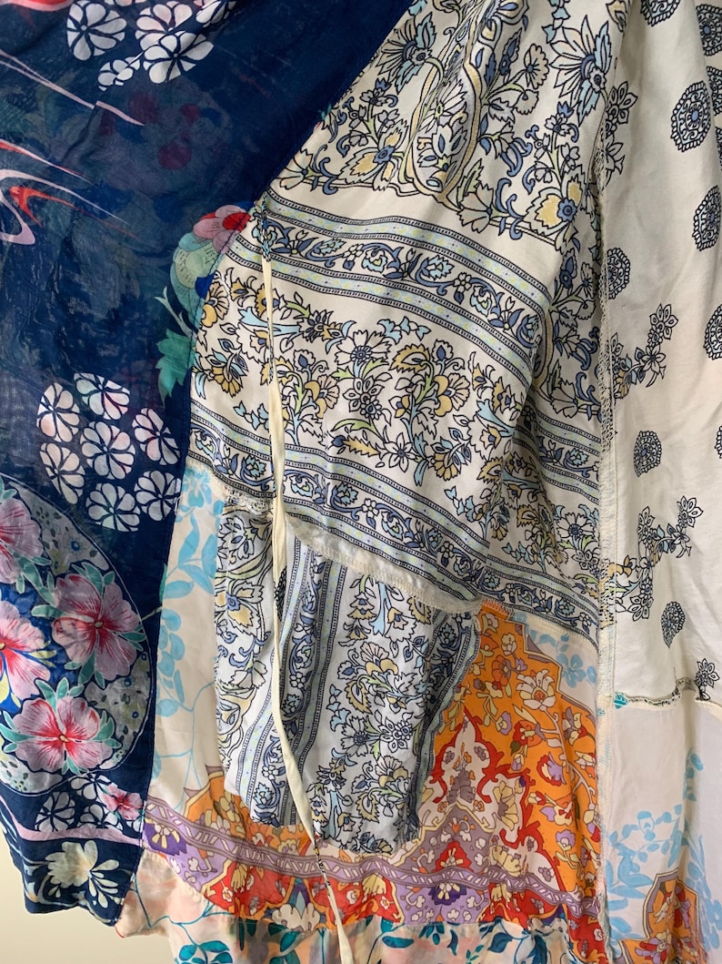 May include: A patchwork garment featuring a variety of floral and paisley patterns in shades of blue, white, orange, and purple. The garment appears to be made of lightweight fabric, possibly a kimono or a similar style of cover-up.